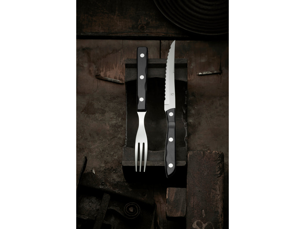 Sort bestik med stilrent design bestående af en gaffel og en kniv i rustfrit stål med sort håndtag placeret på en rustik baggrund