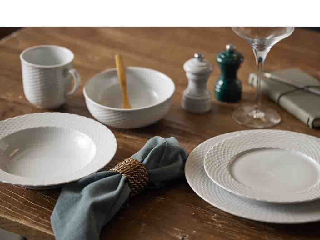 Peugeot Bistrorama saltkværn i grøn placeret på et rustikt træbord blandt hvidt porcelæn, en grøn serviet og et glas.