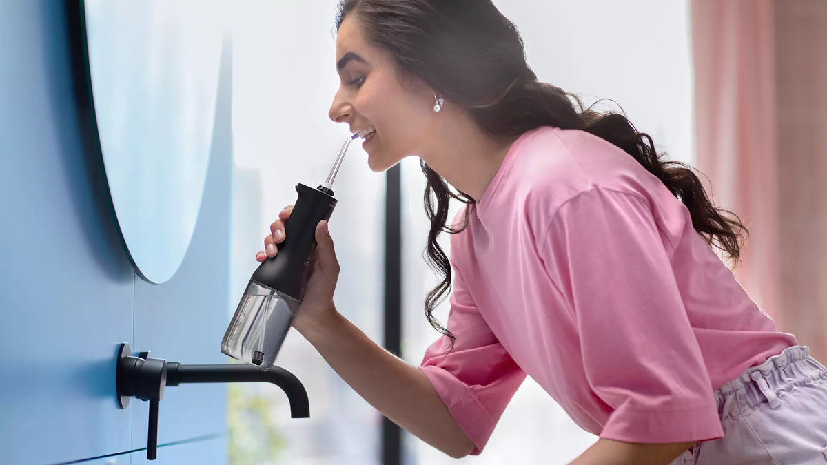 Kvinde i lyserød bluse bruger Philips HX3826/33 Sonicare Power Flosser 3000 ved et vandhaner i et lyst rum med moderne indretning