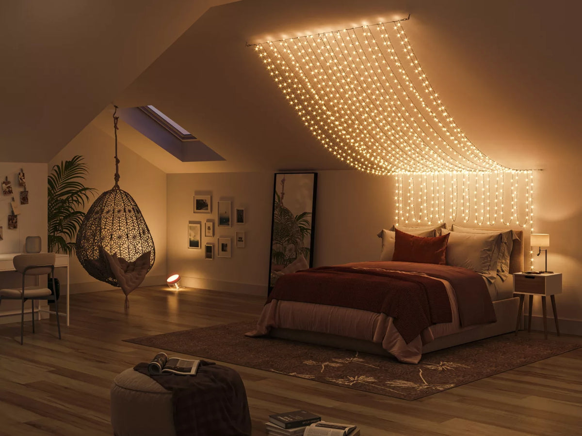 Philips Hue Festavia lyskæde med 250 LED'er hængende i en dekorativ form over en seng i et indbydende soveværelse med varme farver og moderne indretning