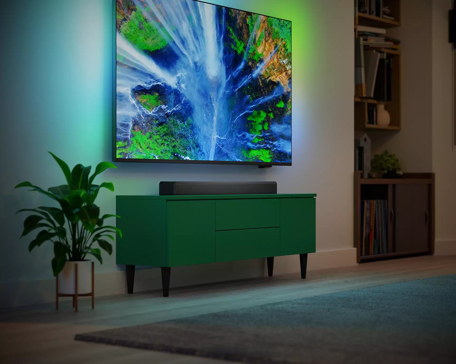 Philips TAB5109/10 soundbar placeret under en vægmonteret tv-skærm i et moderne stueindretning med en grøn stueplante i forgrunden og bløde belysningseffekter fra tv'et