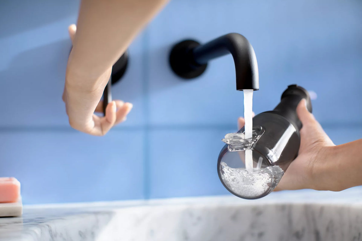 En hånd hælder vand i en Philips HX3826/33 Sonicare Power Flosser 3000 med en sort vandhane i baggrunden og en marmoroverflade i forgrunden