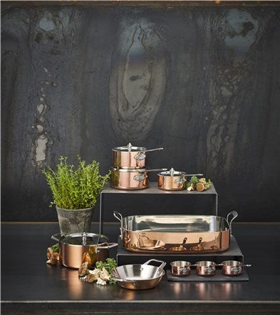 Scanpan bradepande i kobber 35x24cm fra Maitré D' placeret blandt variasjoner af kobbergryder og friske urter på en mørk overflade