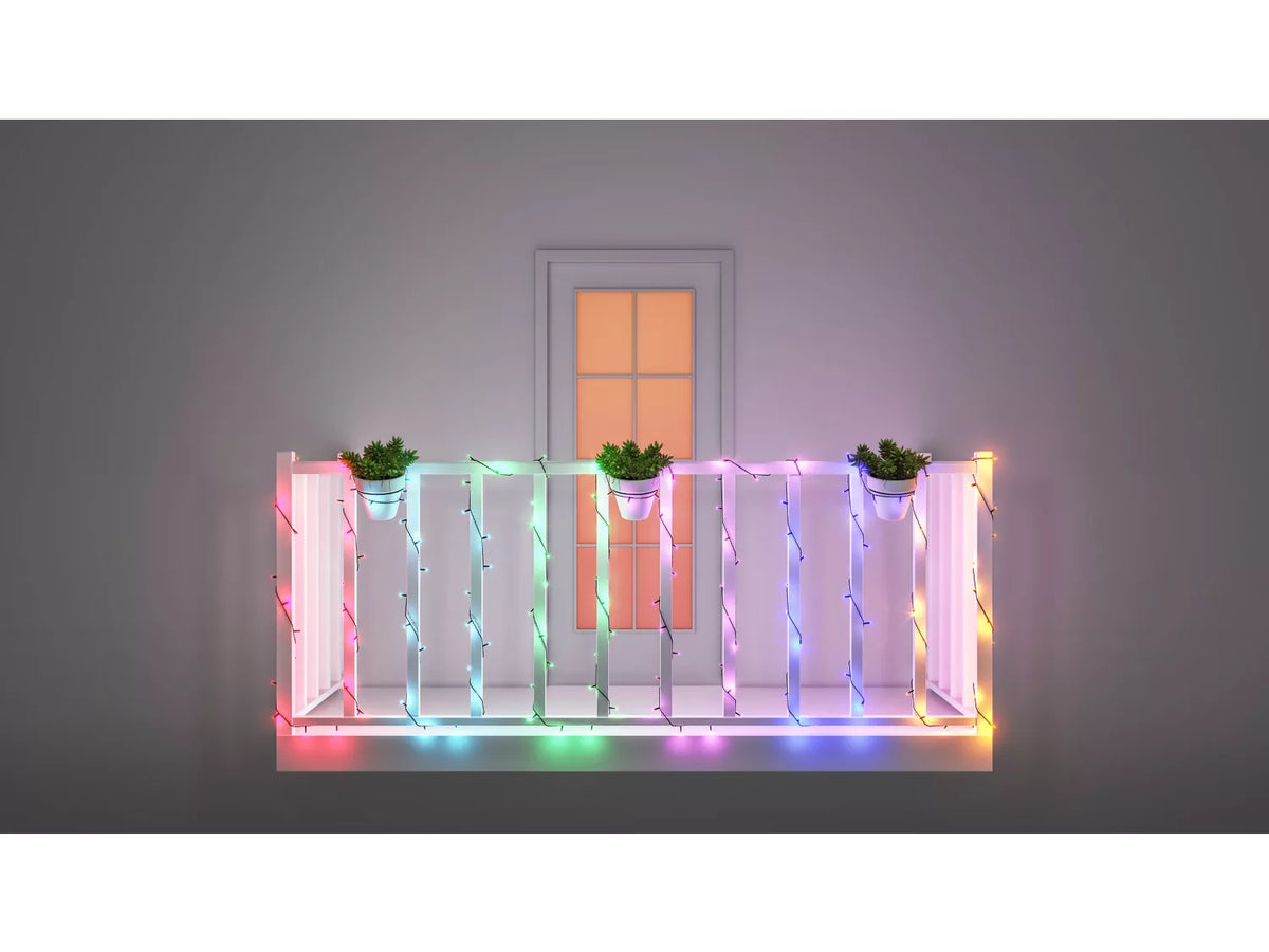 Billede af en hvid rækværk balkon med farverig WIZ Fairy light lyskæde på 20 meter der er dekoreret med potteplanter og en dør baggrunden der har et vindue. Lyskæden har flere forskellige farver som skaber en festlig og indbydende atmosfære.