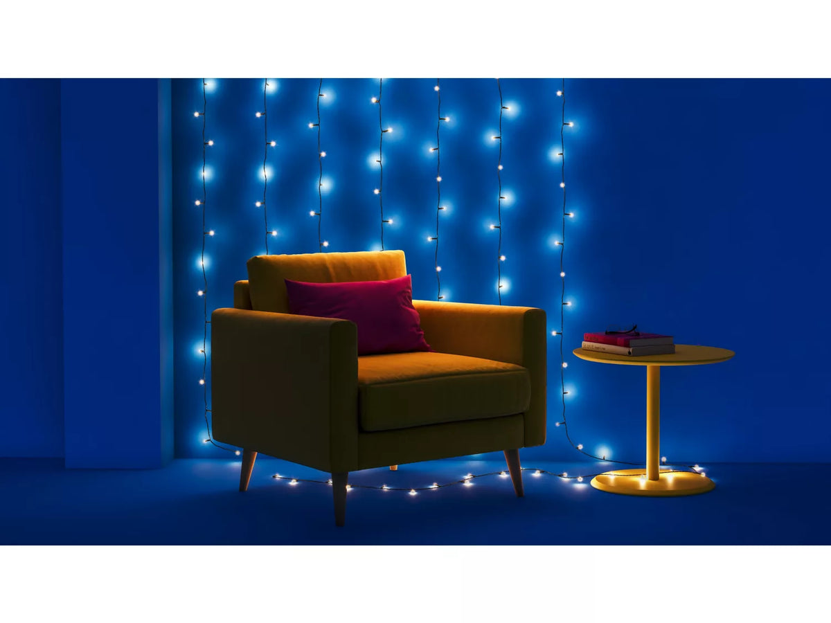 WIZ Fairy light lyskæde 20 m med klare og blå LED-lamper hængende i et stilfuldt rum med en grønlig sofa og et rundt gult bord der bærer bøger