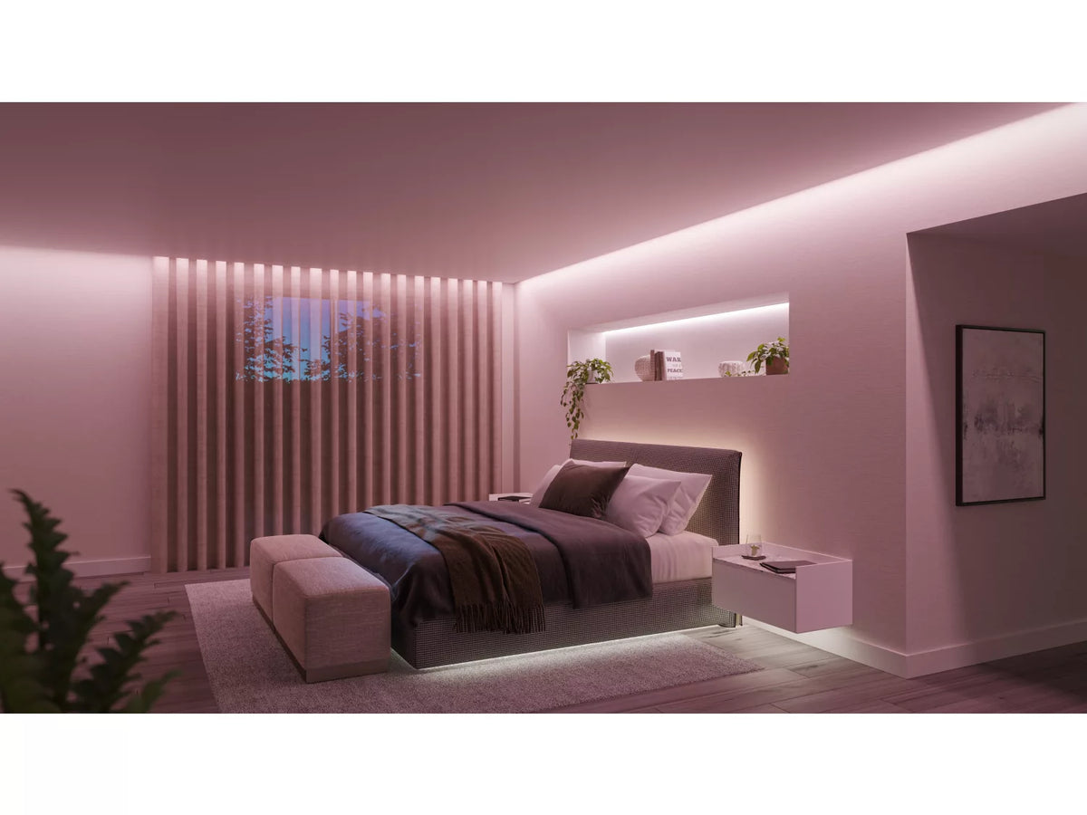 Billede af et soveværelse oplyst af Philips HUE Solo lysstribe på 3 meter med bløde lyse nuancer der skaber en hyggelig atmosfære sengen er placeret centralt med en sengegavl i moderne design og små dekorative planter på hylden bagved samt en natbordslampe ved siden af sengen
