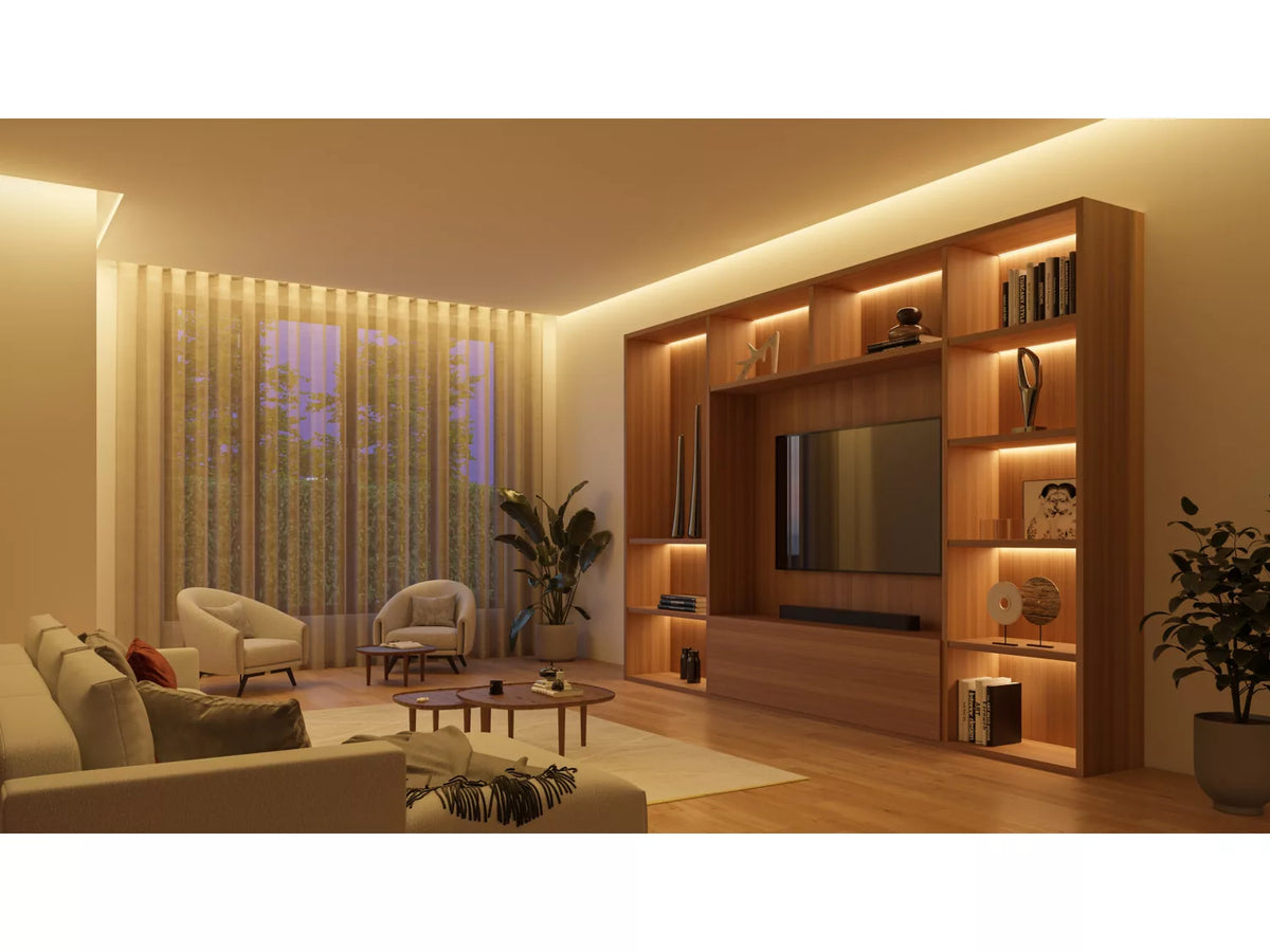 Stue med bløde farver og moderne møbler der inkluderer en sofa, to lænestole og et rundt sofabord hvor Philips HUE Solo lysstribe på 3 meter skaber en stemningsfuld belysning omkring en tv-væg med bøger og dekorative genstande