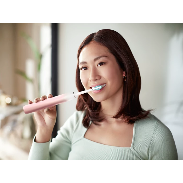 Kvinde der børster tænder med en Philips Sonicare DiamondClean 9000 Series elektrisk tandbørste i en lys stue med en moderne atmosfære