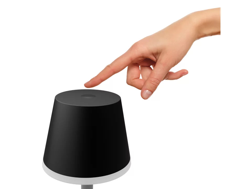 Hånd der trykker på toppen af en sort Philips Hue Go bærbar bordlampe med cylindrisk form