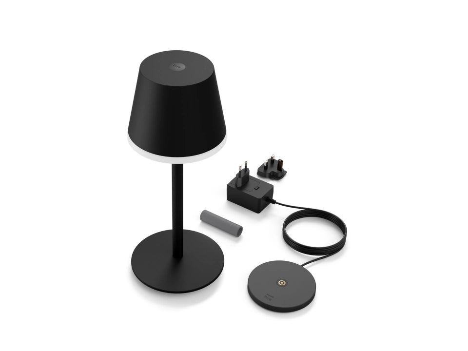 Billede af en Philips Hue Go bærbar bordlampe i sort farve med en rund base og en skærm i en lampetop. Lampen står sammen med en adapter, en ledning og to stik til strømforsyning.