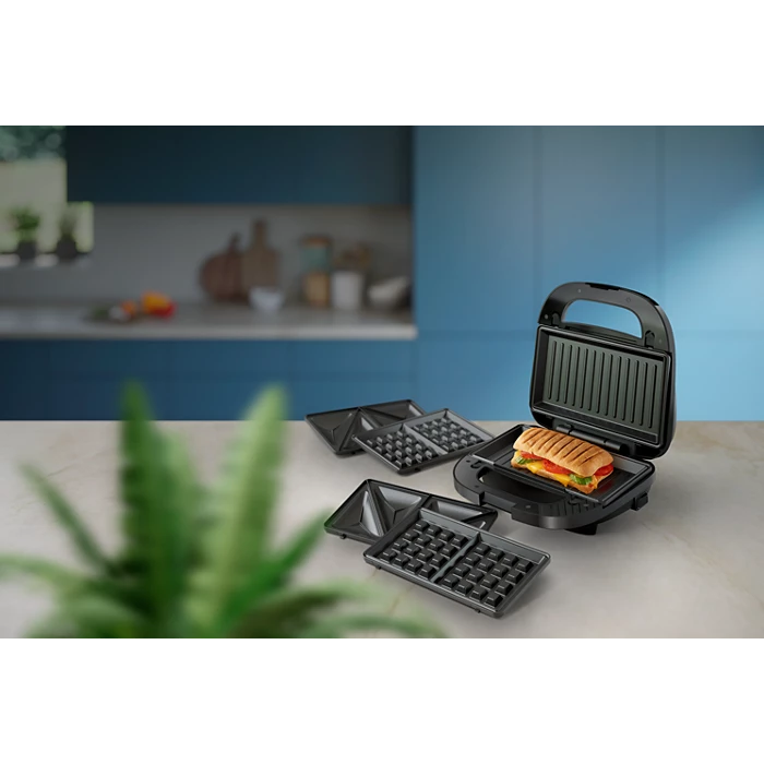 Philips HD2350/80 sandwichtoaster med en smukt tilberedt sandwich indeni og udskiftelige plader til både sandwich og vafler placeres på et køkkenbord med en moderne baggrund og grønne planter i forgrunden