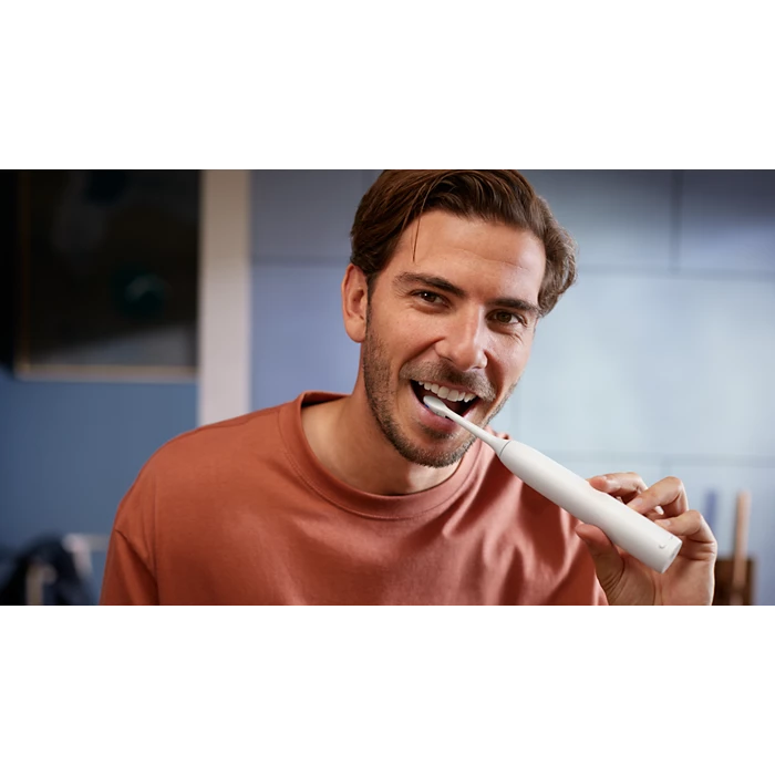 Mand i en rustfarvet t-shirt børster sine tænder med en Philips Sonicare 5300 genopladelig tandbørste i et moderne badeværelsesmiljø