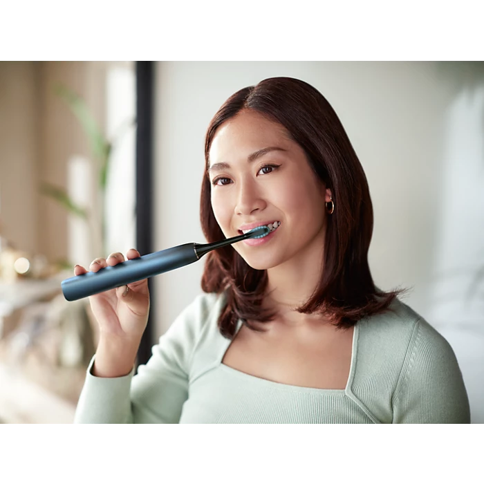 Kvinde med brune hårstrå bruger en Philips Sonicare DiamondClean 9000 Series elektrisk tandbørste i specialudgave mens hun smiler