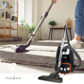 Nedis støvsuger med pose 700W VCBG250GY i brug på et tæppe i et lyst rum med en plante i baggrunden og en person iført jeans der bruger støvsugeren