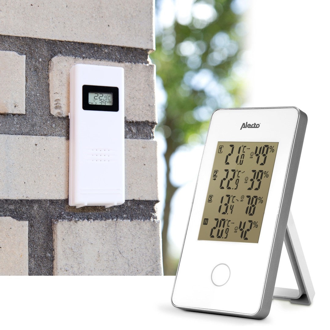 Billede af Alecto WS-1330 vejrstation med tre sensorer enheden er placeret på en murstensvæg til venstre og en digital skærm med temperatur og fugtighedsværdier til højre skærmen viser forskellige målinger som indendørs og udendørs temperatur samt luftfugtighed