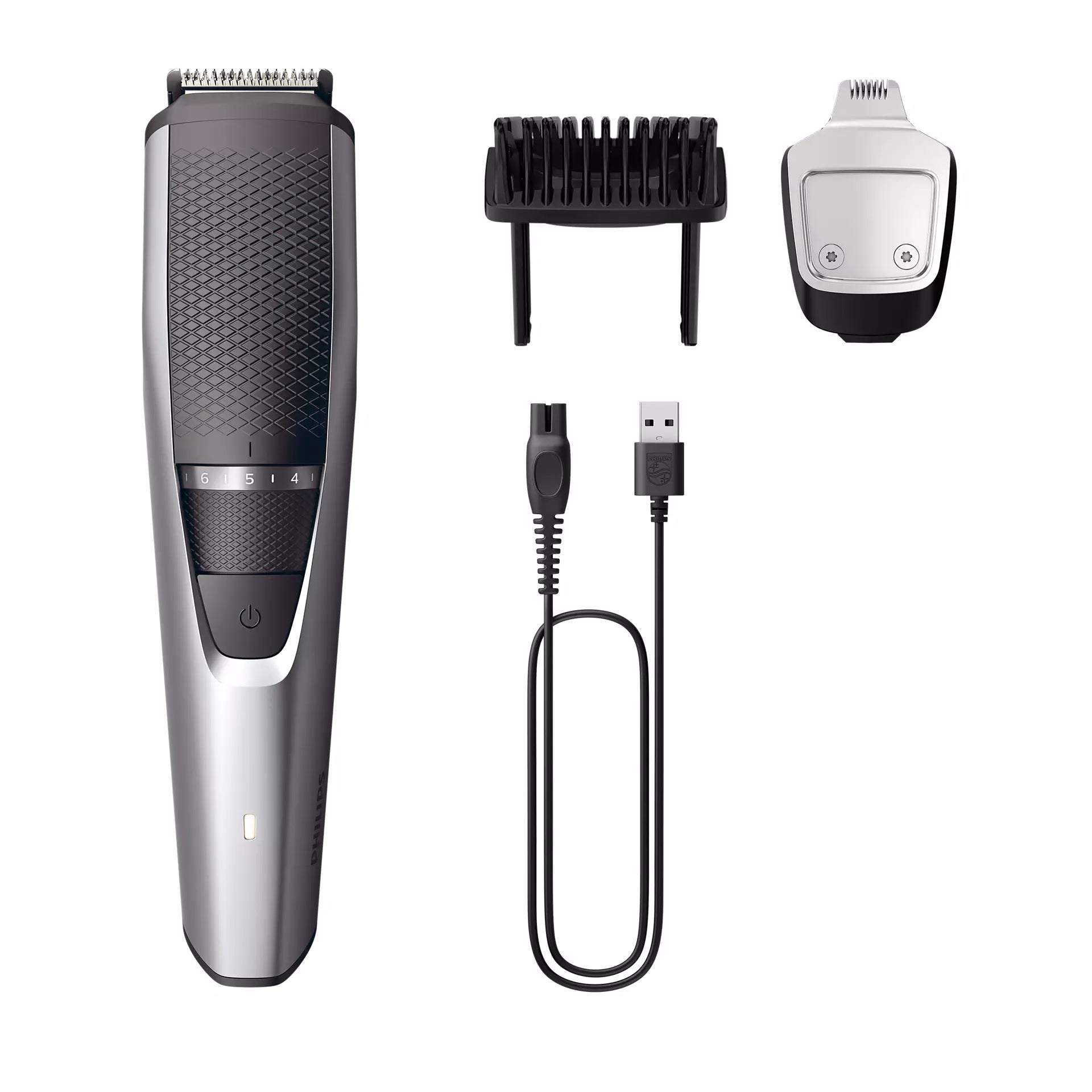 Philips BT3239/15 skægtrimmer serie 3000 ligger i midten af billedet med en sort og sølv farve. Trimmeren har en justerbar længdeindstilling i tal fra 1 til 5. Til venstre ses en sort kam til justering af hårlængde og til højre en prik med sølv og sort design, som er trimmerens hoved. Nederst til højre er der et USB-ladekabel.