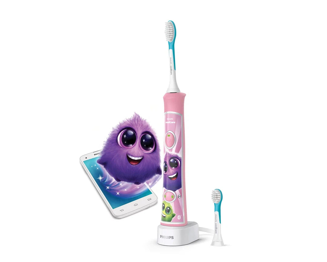 Billede af Philips Sonicare HX6352/42 eltandbørste til børn i pink med farverige motiver og en tilhørende app, der viser en sød lilla karakter og et smartphone-logo. Eltandbørsten står på en ladestation med en ekstra børstehoved ved siden af.