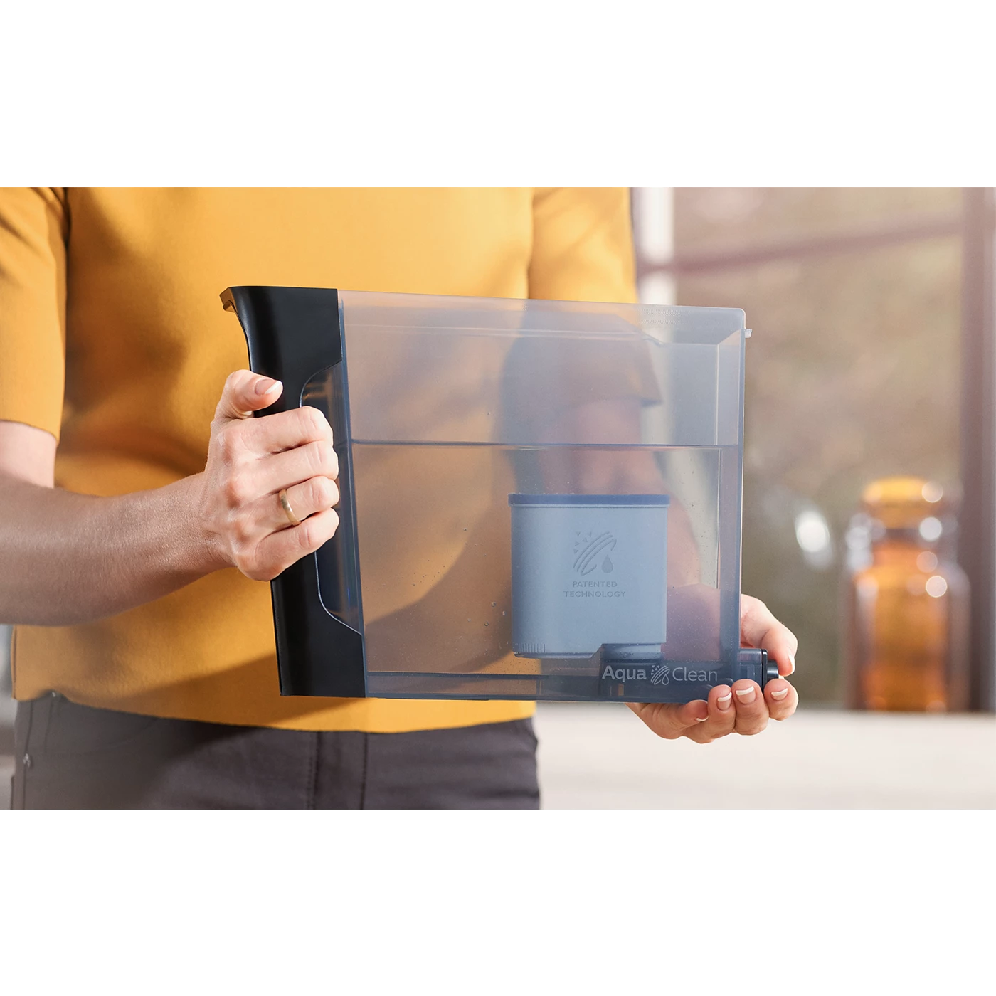 Person holder et gennemsigtigt vandfilter fra Philips CA6903/10 med en blød blå tanke indeni i et lyst køkkenmiljø