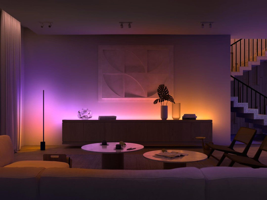 Philips HUE Gradient lightstrip forlænger på 1 meter installeret i et moderne rum med blødt lys i nuancer af lilla, orange og gult der skaber en hyggelig atmosfære med en sofa, stuebord og en dekorativ plante i en vase