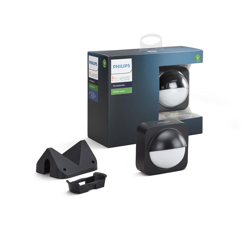 Produktbillede af Philips Hue udendørssensor pakket sammen med tilbehør inklusive monteringselementer og en sort kasse med gennemsigtigt vindue der viser sensoren.