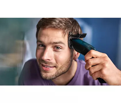 Mand klipper sit hår med Philips HC3505/15 hårklipper viser ansigtet med et smil 13 længdeindstillinger synlig på klipperen baggrund i bløde farver
