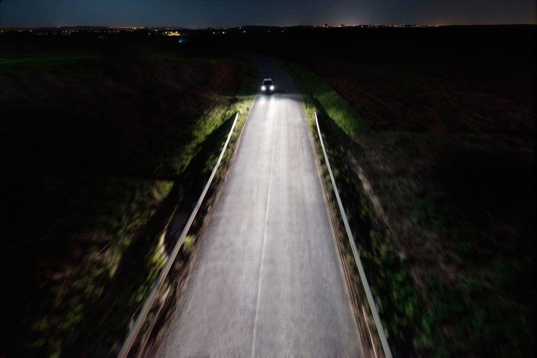 Billede af en bil der kører ned ad en landsbyvej om natten med klart lys fra Philips 12258XVPS2 H1 forlygter X-tremeVision Pro150 der lyser vejen og omgivelserne op