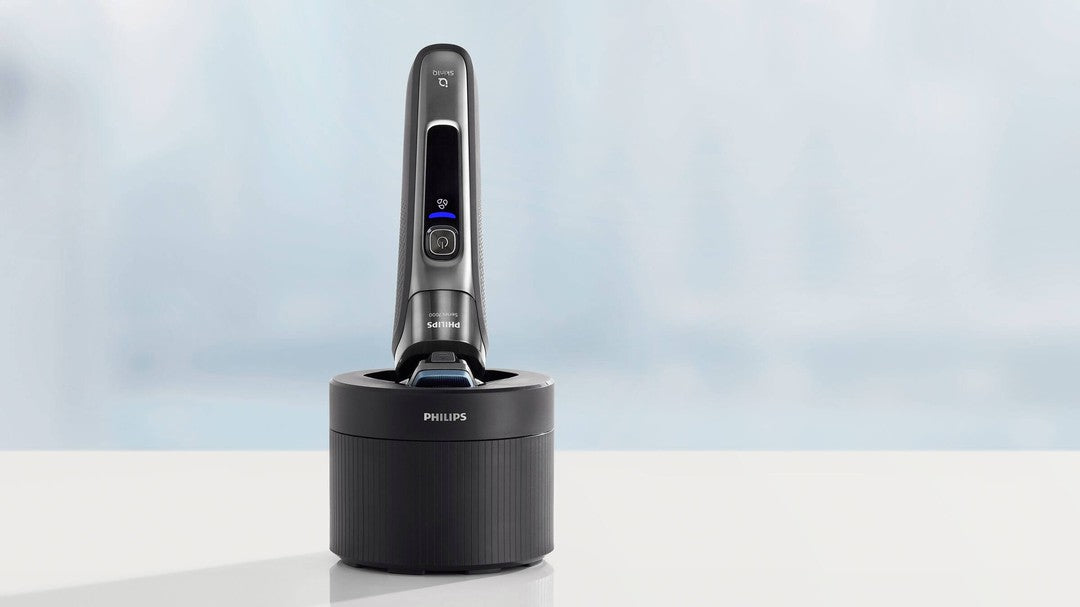 Philips CC12/50 QuickClean rengøringspatron står på en hvid overflade med en slank grå rengøringsenhed i fokus det har en blåt lys og knapper som viser status for enheden