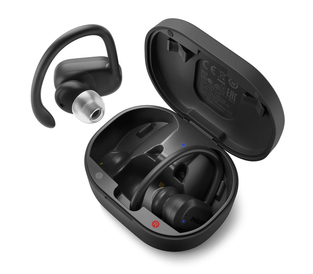 Billede af Philips TAA7306BK/00 True Wireless sportshovedtelefoner sat i en ladestation med et øretelefon med bølgeformet silikonebøjle ved siden af ladestationen med et minimalistisk sort design og tydelige knapper.