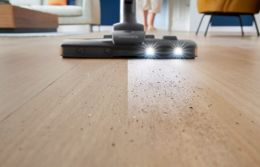Billede af en Philips FC9747/09 PowerPro Expert poseløs støvsuger som rengør et trægulv med synlige støvpartikler på gulvet og lys fra støvsugerens hoved.