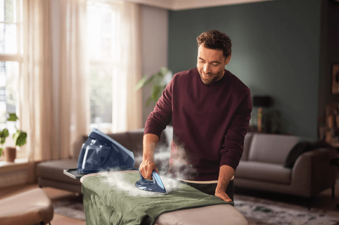 Mand i sweater stryger et grønt tøjstykke med Philips Dampstation PSG7030/20 i et lyst rum med naturligt lys og moderne indretning