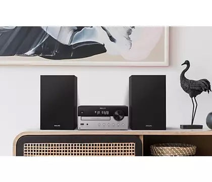 Philips TAM4205/12 minianlæg med Bluetooth står på et TV-møbel med to sorte højtalere på hver side og en minimalistisk surrounddekoration i form af en sort skulptur af en fugl