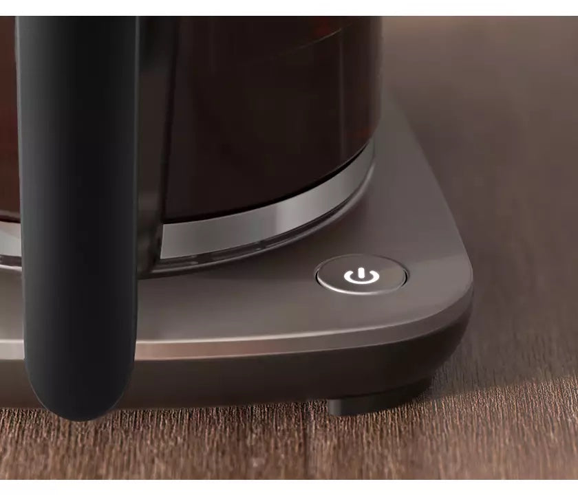 Billede af tænd/sluk knappen på Philips HD5416/60 Café Gourmet Filterkaffemaskine med en moderne designdetalje på en træoverflade