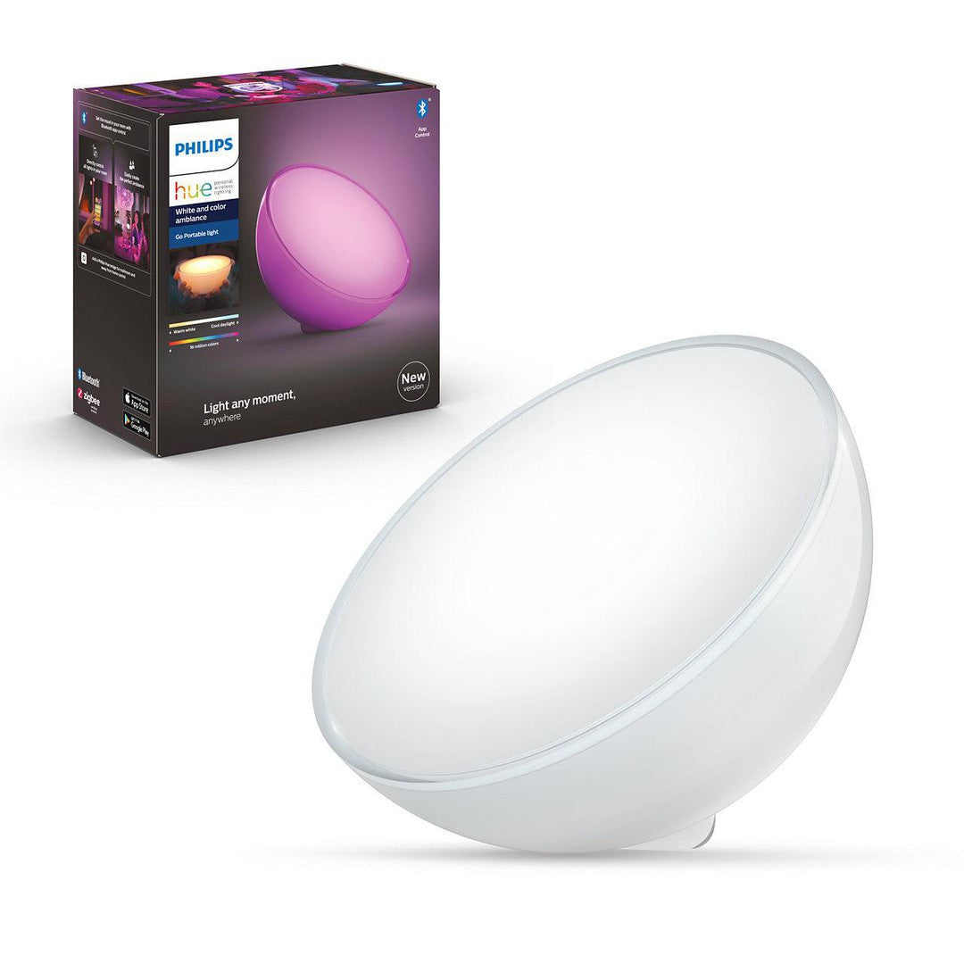 Philips Hue GO Bluetooth bordlampe i oval form med blødt hvidt lys står ved siden af sin emballage der viser lampe i pink og beskriver dens funktioner som trådløs og farvevariabel lampe
