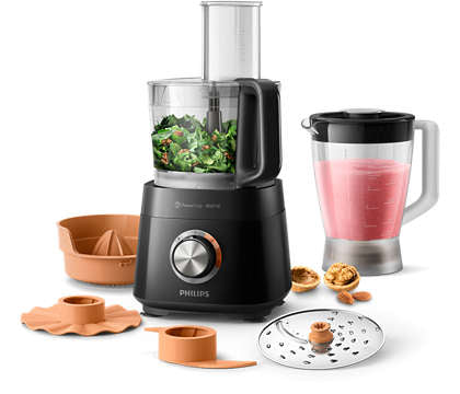 Philips HR7510/10 Kompakt foodprocessor med 800W effekt og 29 funktioner står på en lys overflade med grøntsager i skålen og en smoothie i glasset ved siden af diverse tilbehør som skiver og juicer tilbehør